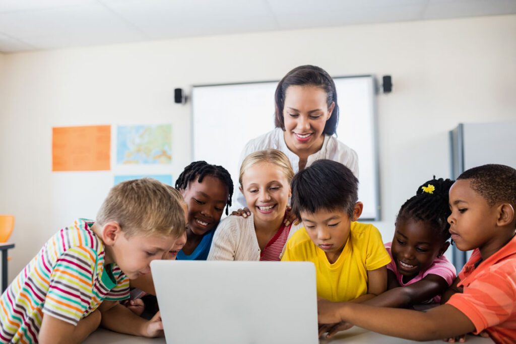 African American female elementary school teacher with her students around a laptop